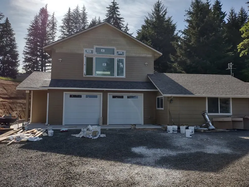Street-level view of a new two-car garage with ADU second story, tan siding and white garage doors, near completion in Eugene, Oregon.