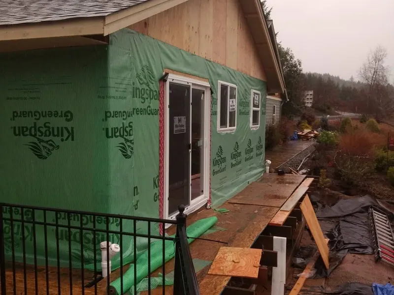 Bright green Kingspan GreenGuard weather barrier wrap installed on a new home addition with deck framing visible in the foreground.