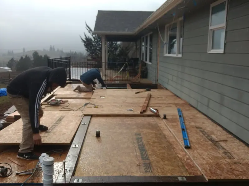 Two Red Umbrella workers installing OSB subfloor panels on a raised home addition platform on a foggy Pacific Northwest morning.
