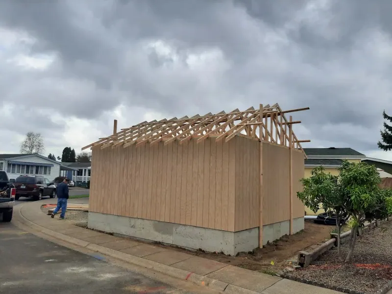 Small detached garage under construction with T1-11 siding and fresh roof trusses being installed in a suburban Eugene, Oregon neighborhood.