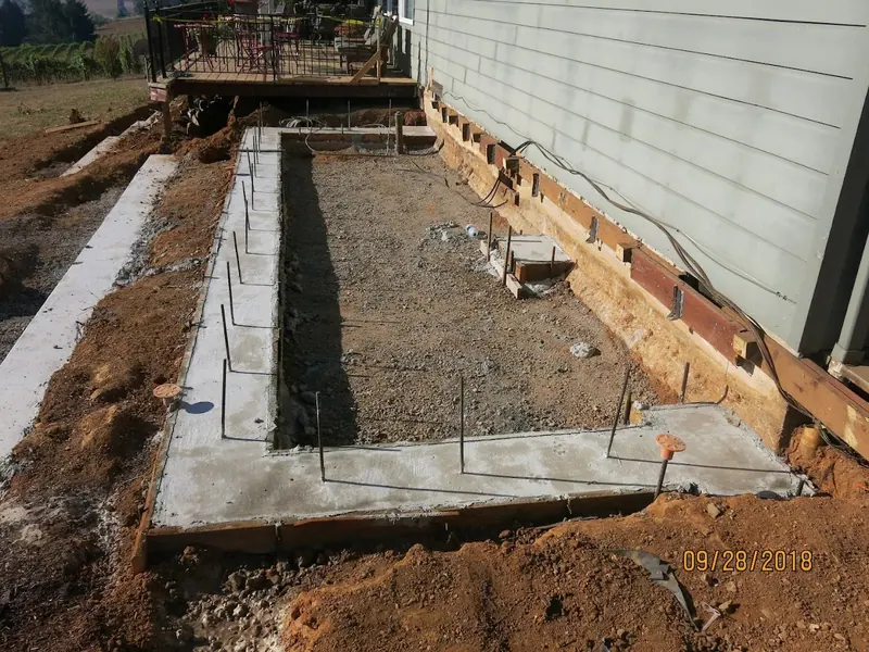 Freshly poured concrete stem wall foundation footings with rebar dowels for a home addition project, dated September 2018, by Red Umbrella.