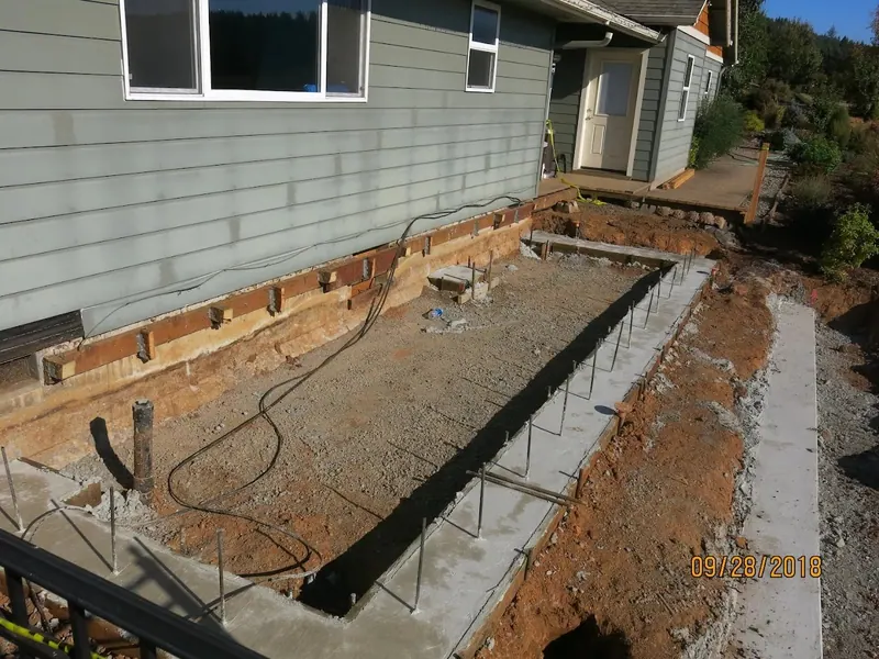Foundation excavation with rebar forms for a home addition beside an existing gray lap-siding house, photographed during construction by Red Umbrella.