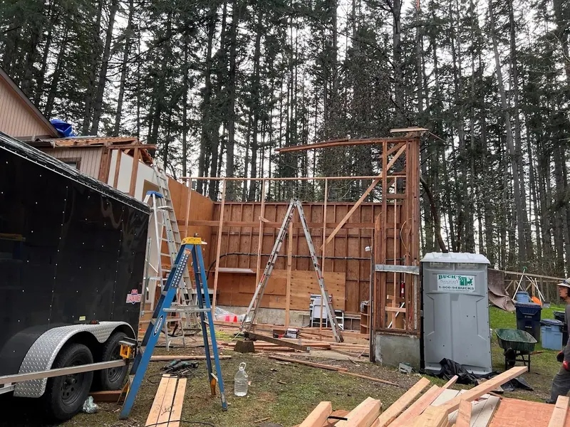 Tall wall framing for a garage or shop addition showing a large bay door opening in a forested Eugene Oregon setting, Red Umbrella construction.