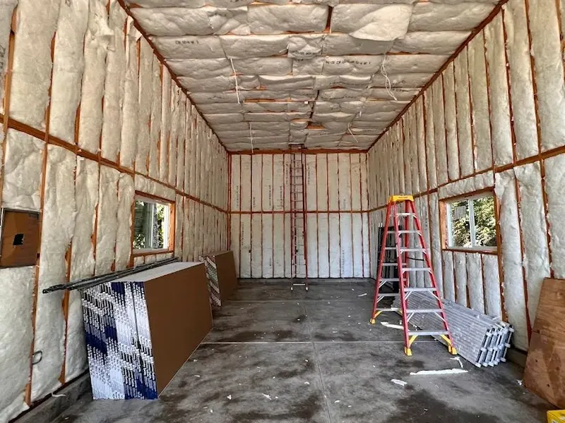 Newly insulated garage interior with white batt insulation in orange metal stud framing, ready for drywall, built by Red Umbrella.