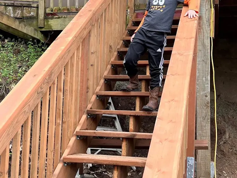 Freshly built cedar deck staircase with vertical baluster railing, with a child on the steps to show scale during construction in Eugene.