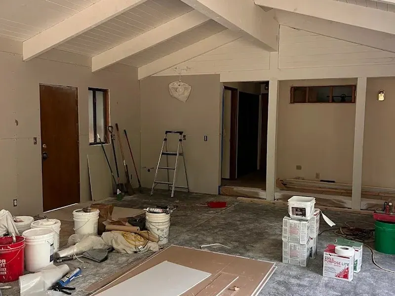 The same vaulted open-concept great room before renovation by Red Umbrella, showing bare concrete floors and existing rafter ceiling structure.